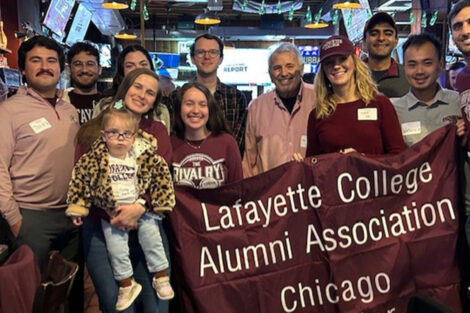 A group of alumni stand with a Lafayette flag that reads Lafayette College Alumni Association Chicago