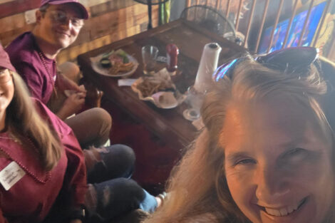 A woman is seated at a table with a group of people. She is taking a selfie.