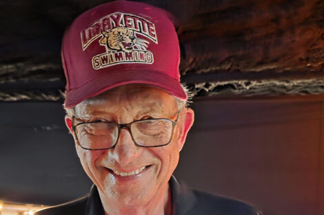 A man smiles at the camera. He is wearing a Lafayette swimming hat.