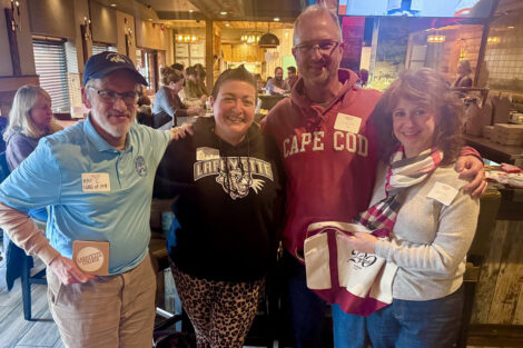 Alumni are standing at a bar and are smiling at the camera.